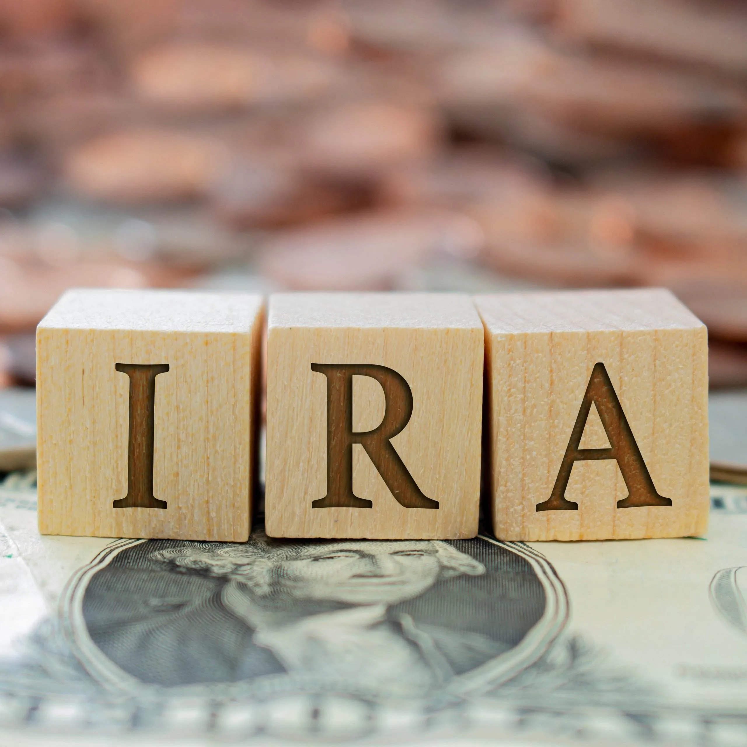 Three wooden blocks sit next to each other on a pile of cash and coins. The blocks contain the letters 