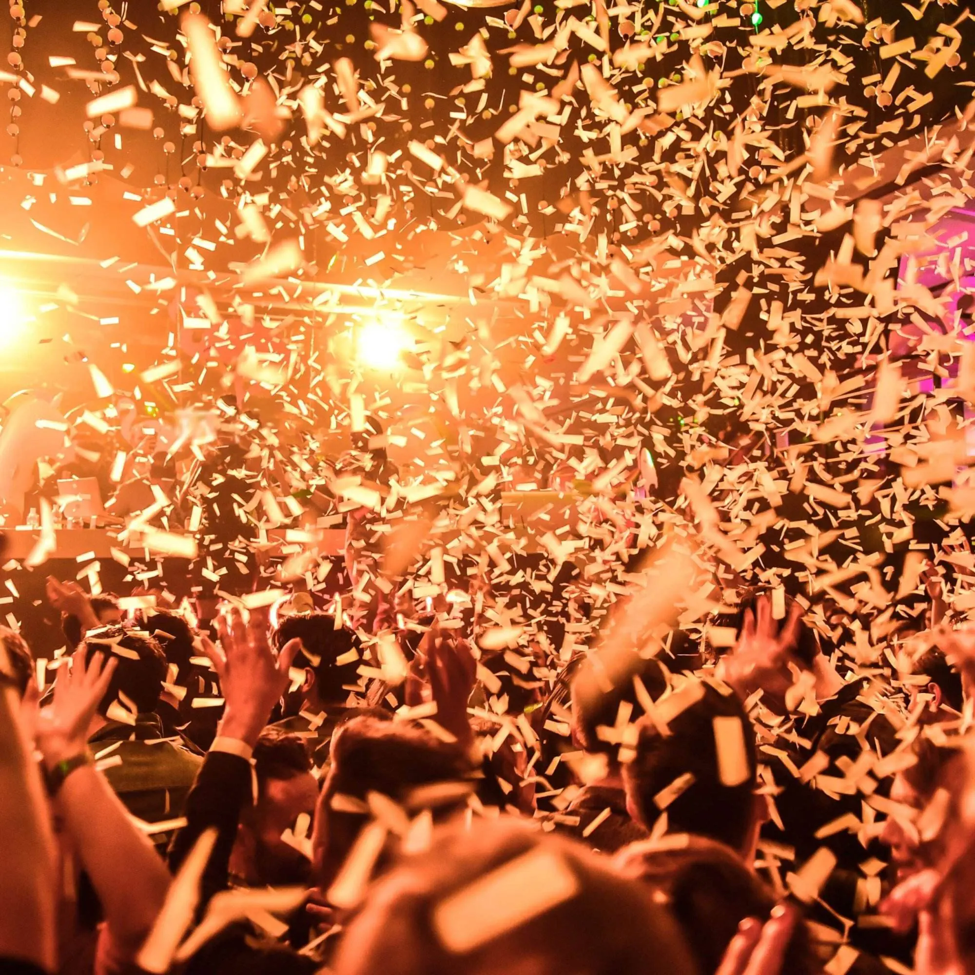 Bright orange lights and a flurry of confetti cover a packed event venue where everyone is raising their hands.